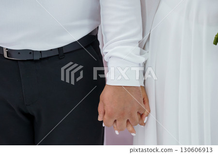 Close-up of Couple Holding Hands, Wedding Day Romance, Black Suit, White Dress, Celebration, Love, Formal Attire, Neutral Background, Stylish. 130606913
