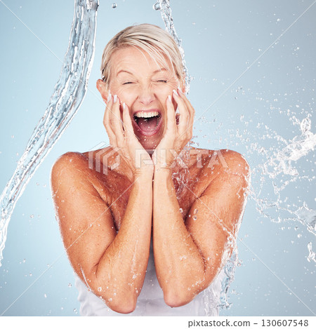 Skincare, excited and portrait of a woman with a water splash isolated on a blue background. Self care, happy and face of an elderly beauty model cleaning her body for wellness on a studio backdrop 130607548