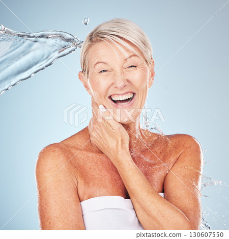 Smile, shower and portrait of a woman with a water splash isolated on a blue background in studio. Grooming, hygiene and face of an excited senior model with body and self care on a backdrop 130607550