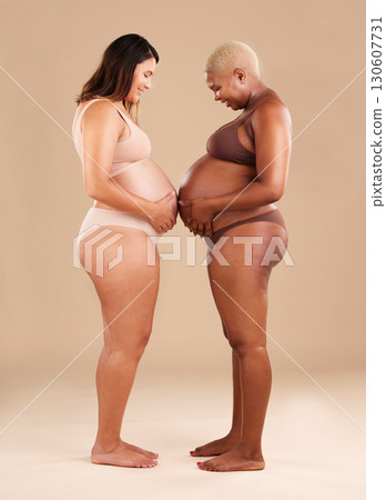 Two women, pregnant and belly touch in studio for support, bonding and friends by background. Young future mother, pregnancy and happy with solidarity, diversity and care for wellness, health or hope Two women, pregnant and belly touch in studio for support, bonding and friends by background. Young future mother, pregnancy and happy with solidarity, diversity and care for wellness, health or hope 130607731