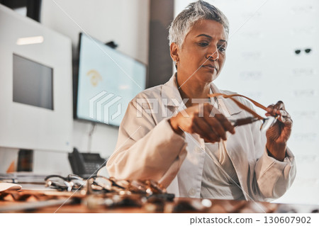 Elderly optometrist woman, glasses and design for focus, vision or frame planning at desk in clinic. Senior optician, spectacle designer and eye care in workplace for fashion, small business and goal 130607902