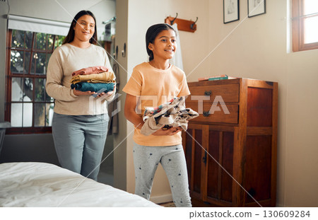 Little girl, mom and helping with laundry for chores, clothing or folded washing with smile at home. Happy child walking with mother carrying clean clothes for hygiene, housework or routine indoors 130609284