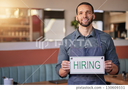 Recruitment, portrait or man with a hiring sign for job vacancy offer in cafe or small business store. Hospitality, labour shortage or happy entrepreneur smile with an onboarding message to hire 130609331