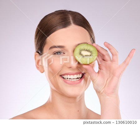 Woman, face and hand with kiwi for skincare nutrition or healthy diet against gray a studio background. Portrait of happy female smile with fruit for organic facial treatment or natural cosmetics Woman, face and hand with kiwi for skincare nutrition or healthy diet against gray a studio background. Portrait of happy female smile with fruit for organic facial treatment or natural cosmetics 130610010