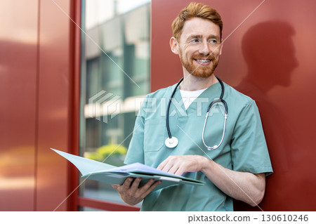 Male healthcare worker in scrubs holding open folder 130610246