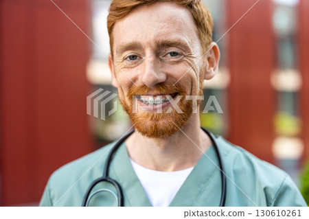 Smiling man doctor in scrubs with ginger beard outdoors Smiling man doctor in scrubs with ginger beard outdoors 130610261