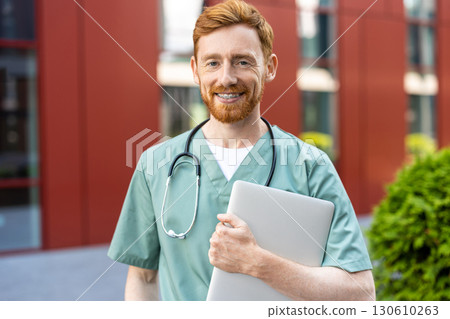 Man doctor with red hair and beard carrying closed laptop Man doctor with red hair and beard carrying closed laptop 130610263