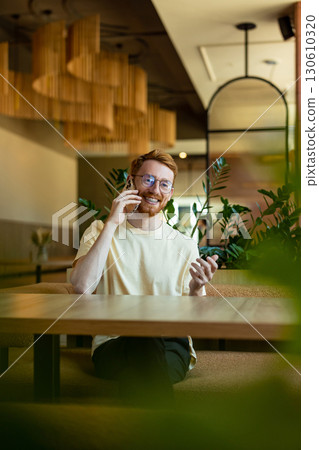 Red-haired man communicating on phone in cozy cafe 130610320