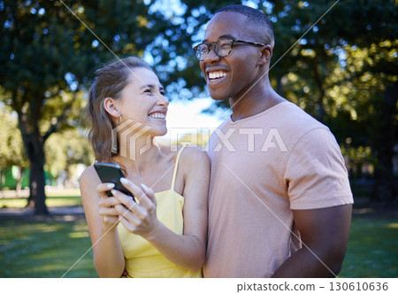 Comedy, laughing and interracial couple with a phone in nature, funny communication and smile at a meme. Comic, streaming and black man and woman reading a joke on a mobile in a park in France 130610636