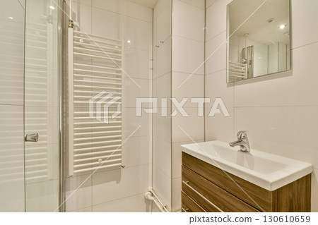 A sleek and contemporary bathroom featuring white tiles and warm wooden accents, enhancing the overall aesthetic appeal and functionality. A sleek and contemporary bathroom featuring white tiles and warm wooden accents, enhancing the overall aesthetic appeal and functionality. 130610659