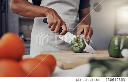 Hands, food and cooking with a man cutting a green pepper in the kitchen on a wooden chopping board. Salad, health and diet with a male chef preparing a meal while standing alone in his home 130610863