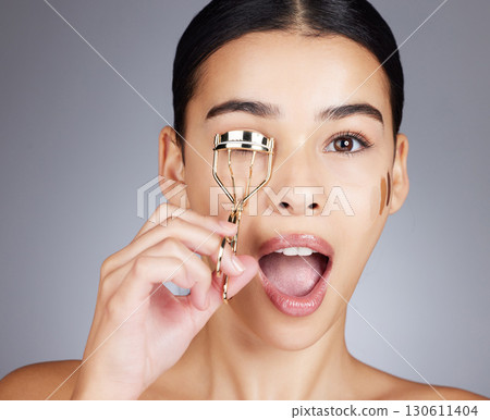 Wow, face and woman with eyelash curler in studio isolated on a gray background. Portrait, makeup surprise and cosmetics of female model with tool or product to curl eyelashes for beauty aesthetics. Wow, face and woman with eyelash curler in studio isolated on a gray background. Portrait, makeup surprise and cosmetics of female model with tool or product to curl eyelashes for beauty aesthetics. 130611404
