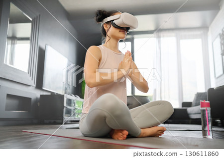 VR, meditation and fitness with a woman using a headset to access the metaverse in her home for health. Virtual reality, yoga and exercise with a young female yogi meditating in her house using 3d ai VR, meditation and fitness with a woman using a headset to access the metaverse in her home for health. Virtual reality, yoga and exercise with a young female yogi meditating in her house using 3d ai 130611860