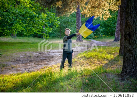 Ukrainian boy with waving flag and praying to stop the war in Ukraine in a field at sunset. War of Russia against Ukraine. Stop War 130611888