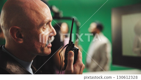 Man, director and radio with green screen for action, scene or instruction in production studio. Male person, producer or manager talking with signal or cut for take, cue or special effects in set Man, director and radio with green screen for action, scene or instruction in production studio. Male person, producer or manager talking with signal or cut for take, cue or special effects in set 130612328