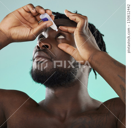 Black man, studio and eye drop for health vision, wellness and self care by blue backdrop for morning routine. African gen z model, eyes and product for healthcare, medicine and medical serum bottle 130612442