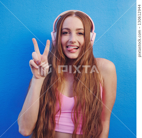 Music, peace and tongue with the portrait of a woman on a blue background while listening to the radio. Face, hand and headphones with an attractive young female streaming an audio playlist or song Music, peace and tongue with the portrait of a woman on a blue background while listening to the radio. Face, hand and headphones with an attractive young female streaming an audio playlist or song 130612944