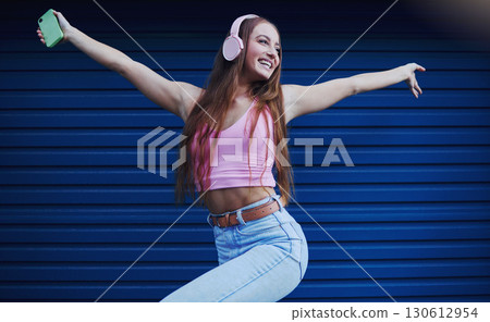 Woman, headphones and dancing outdoor for celebration, achievement and streaming music for fun. Young female, lady or headset for radio, listen to audio or songs with confident girl and casual outfit 130612954