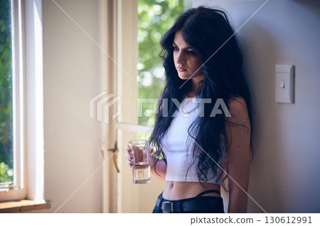 Mental health, depression and sad woman thinking with water, stress and anxiety in a house. Depressed, lonely and goth girl with a drink, emotional and comtemplating problems in the lounge of home 130612991