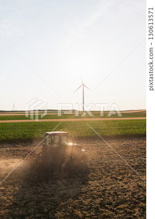 Agricultural tractor is working on the field with wind turbines. Aerial view. 130613571