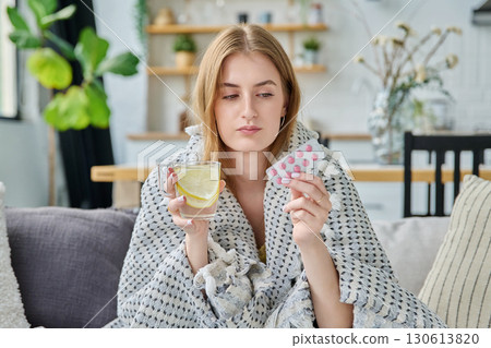 Young woman with fever sick in summer, sitting at home with pills cup of hot tea 130613820