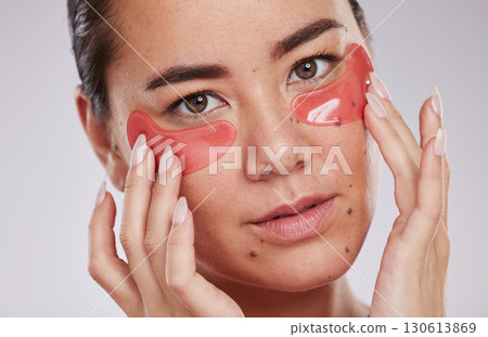 Skincare, face and woman with eye patches in studio isolated on a gray background. Dermatology, cosmetics and portrait of young female model with facial pads or products for beauty or skin treatment. Skincare, face and woman with eye patches in studio isolated on a gray background. Dermatology, cosmetics and portrait of young female model with facial pads or products for beauty or skin treatment. 130613869