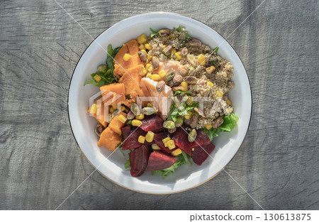 Top view of Delicious Quinoa Salmon Poke bowl garnished with Leaves salad, Beetroot, Sweet potato, Sweet corn and Pistachio. 130613875