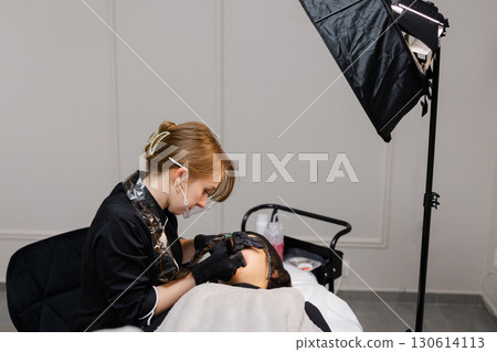 Beautician performing permanent makeup treatment on lips of client lying on couch 130614113
