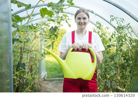 Pregnant woman watering plants in greenhouse with watering can 130614320