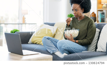 Black woman, watching and movie on a laptop eating popcorn on a living room couch. Scared female person, home lounge and online series with film snack and food with video on computer in a house 130614794