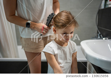 Mother braiding her daughter hair in the bathroom before going to school or kindergarten. Concept of morning preparation, care and family routine in childhood. 130615056