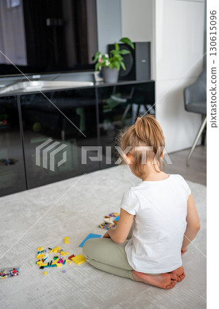 Little girl sitting on the floor and playing with building blocks in the living room. Concept of early development, creativity and focused play in a home environment. 130615096