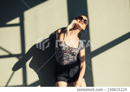 A young woman with a long ponytail stands against the wall, touching the screen of her phone 130615124