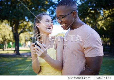 Interracial, social media and couple with a phone in nature, funny communication and laughing at meme. Comic, streaming and black man and woman reading a joke on a mobile in a park in France 130616155