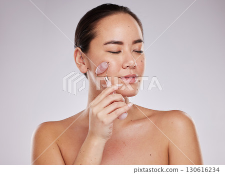 Face skincare, eyes closed and woman with jade roller in studio isolated on a gray background. Beauty cosmetics, dermatology and young female model with rose quartz stone or product for healthy skin 130616234