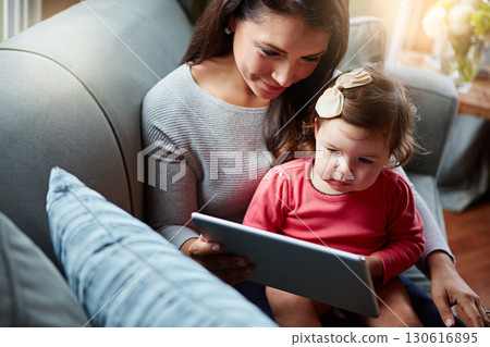 Mother, baby and tablet on sofa watching educational video online on streaming service in home. Love, family time and woman with girl child smile on couch to watch kids movie or cartoon on website. 130616895