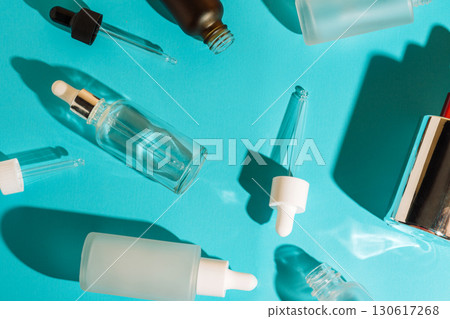Glass cosmetic dropper bottles and pipettes on blue background. Skincare and beauty packaging concept. 130617268
