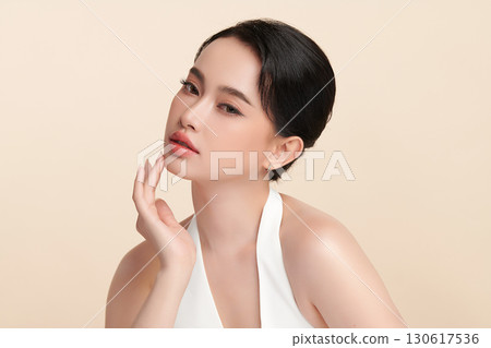 A beautiful young Asian woman with clean, fresh skin against a beige background. Skincare, facial treatment, cosmetology, beauty, and spa. An elegant portrait of an Asian woman. 130617536