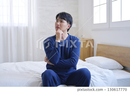 A man in his 20s sitting on a bed thinking A man in his 20s sitting on a bed thinking 130617770