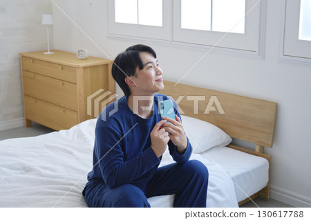 一名 20 多歲的男子想像躺在床上玩智慧型手機 130617788