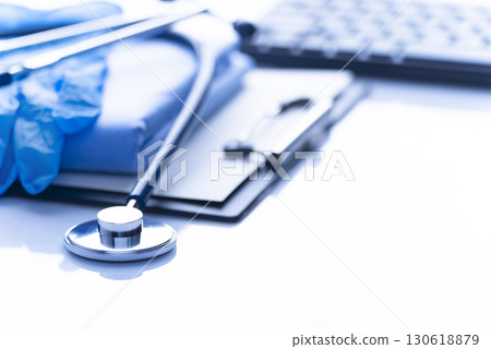 Healthcare medical background with copy-space of stethoscope clipboard, folded overalls, gloves and computer keyboard on white table Healthcare medical background with copy-space of stethoscope clipboard, folded overalls, gloves and computer keyboard on white table 130618879