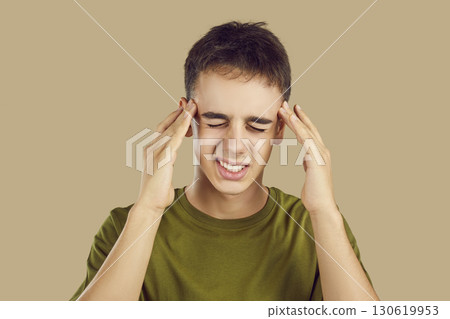 Portrait of a young boy suffering from headache isolated on a studio beige background. Portrait of a young boy suffering from headache isolated on a studio beige background. 130619953