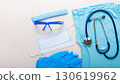 Healthcare background of disposable face mask, gloves, cap, goggles, scrubs and stethoscope laying on table flat lay view 130619962
