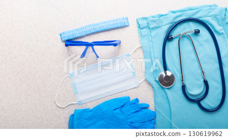 Healthcare background of disposable face mask, gloves, cap, goggles, scrubs and stethoscope laying on table flat lay view 130619962