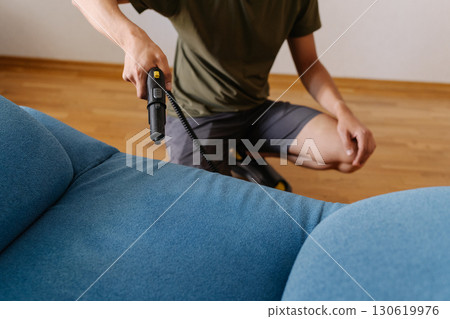 Cropped shot of cleaning service worker using steam cleaner to remove dirt and stains from blue sofa in modern living room, ensuring hygiene and freshness. Concept of easy housekeeping domestic life. Cropped shot of cleaning service worker using steam cleaner to remove dirt and stains from blue sofa in modern living room, ensuring hygiene and freshness. Concept of easy housekeeping domestic life. 130619976