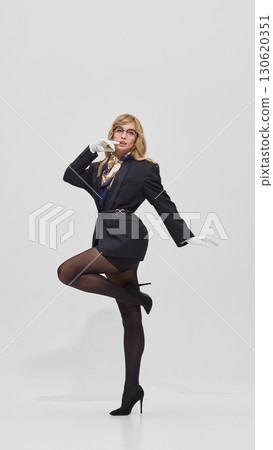 Woman balancing on one leg in black blazer with scarf and white gloves 130620351