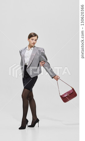 Stylish woman holding red handbag in silver blazer and black skirt posing Stylish woman holding red handbag in silver blazer and black skirt posing 130620366