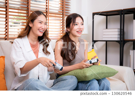 Two asian woman playing video games together with controllers in a cozy living room at home. 130620546