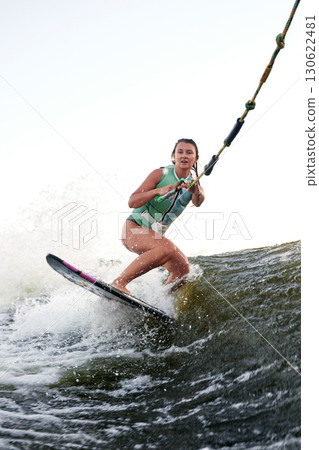 Woman wakeboarding on choppy water holding a rope during a sunny day 130622481