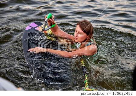 Woman holding a rope on a wakesurf board in water 130622492